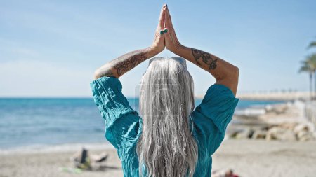 Foto de Mujer de pelo gris de mediana edad haciendo ejercicio de yoga en la playa - Imagen libre de derechos