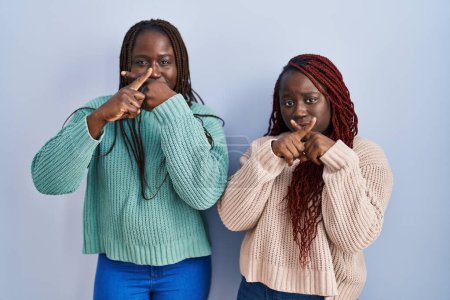 Foto de Dos mujeres africanas de pie sobre la expresión de rechazo de fondo azul cruzando dedos haciendo signo negativo - Imagen libre de derechos