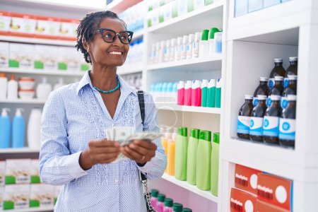 Téléchargez les photos : Middle age african american woman customer smiling confident counting dollars at pharmacy - en image libre de droit