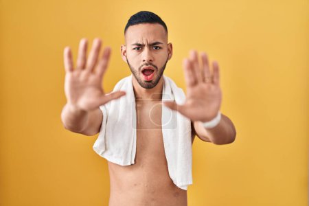 Téléchargez les photos : Jeune homme hispanique debout torse nu avec serviette faisant geste d'arrêt avec les mains paumes de la main, expression de colère et de frustration - en image libre de droit