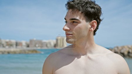 Foto de Joven turista hispano sonriendo confiado de pie en la playa - Imagen libre de derechos