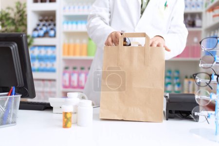 Téléchargez les photos : Non binary man pharmacist putting products on shopping bag at pharmacy - en image libre de droit