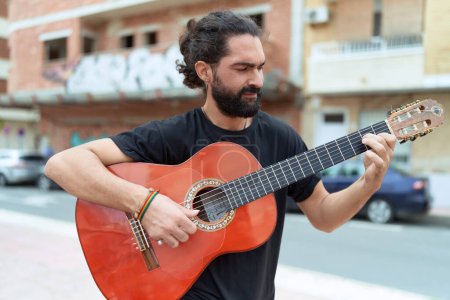 Téléchargez les photos : Jeune homme hispanique musicien jouant de la guitare classique dans la rue - en image libre de droit