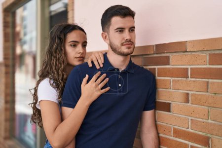 Téléchargez les photos : Jeune couple hispanique s'embrassant debout avec une expression détendue dans la rue - en image libre de droit