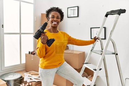 Photo for African american woman holding drill standing on ladder at new home - Royalty Free Image