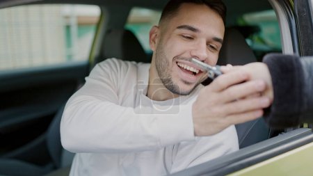 Téléchargez les photos : Jeune homme hispanique souriant réception confiante clé de nouvelle voiture à la rue - en image libre de droit