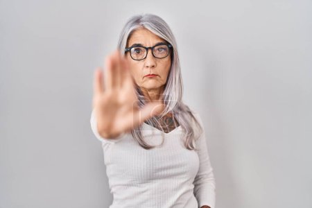 Photo for Middle age woman with grey hair standing over white background doing stop sing with palm of the hand. warning expression with negative and serious gesture on the face. - Royalty Free Image