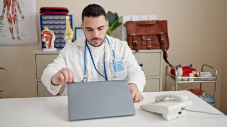 Foto de Joven médico hispano usando laptop trabajando en clínica - Imagen libre de derechos
