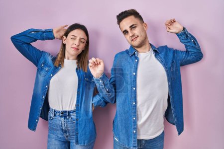 Photo for Young hispanic couple standing over pink background stretching back, tired and relaxed, sleepy and yawning for early morning - Royalty Free Image