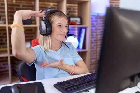 Photo for Young caucasian woman playing video games wearing headphones gesturing with hands showing big and large size sign, measure symbol. smiling looking at the camera. measuring concept. - Royalty Free Image