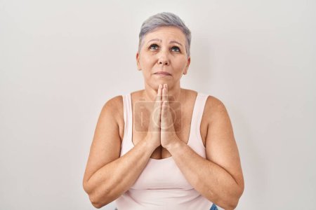 Foto de Middle age caucasian woman standing over white background praying with hands together asking for forgiveness smiling confident. - Imagen libre de derechos