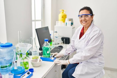 Photo for Middle age hispanic woman wearing scientist measuring liquid at laboratory - Royalty Free Image