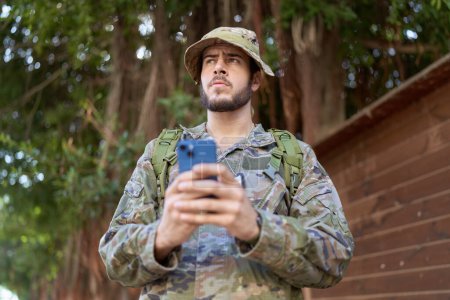Téléchargez les photos : Jeune homme hispanique portant l'uniforme de soldat en utilisant smartphone au parc - en image libre de droit