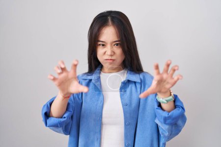 Téléchargez les photos : Jeune femme chinoise debout sur fond blanc souriant drôle faisant griffe geste comme chat, expression agressive et sexy - en image libre de droit