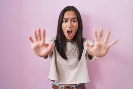 Téléchargez les photos : Young hispanic woman standing over pink background doing stop gesture with hands palms, angry and frustration expression - en image libre de droit
