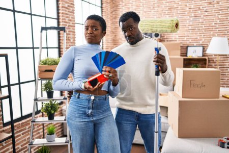 Téléchargez les photos : Jeune couple afro-américain déménageant dans une nouvelle maison en choisissant des murs couleur expression sans idée et confus. concept de doute. - en image libre de droit