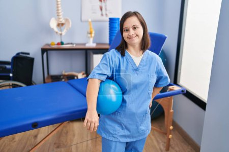 Téléchargez les photos : Femme trisomique portant un uniforme de physiothérapie tenant le ballon à la clinique de physiothérapeute - en image libre de droit