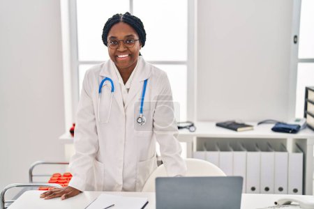 Foto de Mujer afroamericana doctora sonriendo confiada por la mesa en la clínica - Imagen libre de derechos