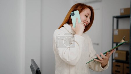 Foto de Mujer pelirroja joven comercio electrónico trabajador de negocios hablando en el teléfono inteligente en la oficina - Imagen libre de derechos