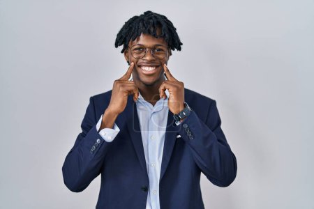 Foto de Joven africano con rastas vistiendo chaqueta de negocios sobre fondo blanco sonriendo con la boca abierta, los dedos señalando y forzando sonrisa alegre - Imagen libre de derechos