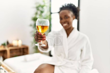 Photo for African american woman wearing bathrobe drinking champagne at beauty salon - Royalty Free Image