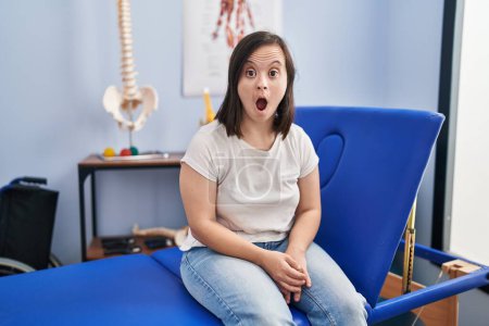 Photo for Hispanic girl with down syndrome at physiotherapy clinic scared and amazed with open mouth for surprise, disbelief face - Royalty Free Image