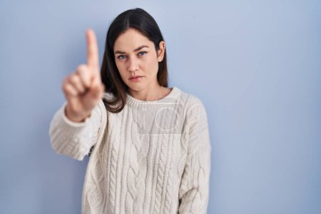 Téléchargez les photos : Jeune femme brune debout sur fond bleu pointant du doigt et l'expression en colère, ne montrant aucun geste - en image libre de droit