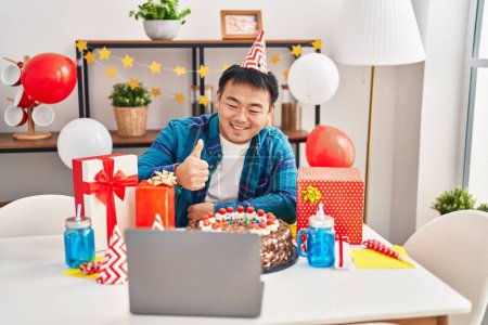 Photo for Young chinese man celebrating birthday with cake doing video call smiling happy and positive, thumb up doing excellent and approval sign - Royalty Free Image