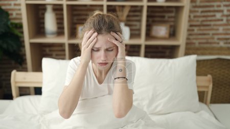 Foto de Mujer rubia joven estresada sentada en la cama en el dormitorio - Imagen libre de derechos