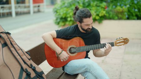 Téléchargez les photos : Young hispanic man musician playing classical guitar sitting on bench at park - en image libre de droit