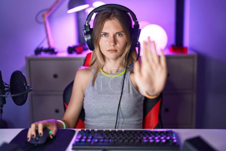 Photo for Blonde caucasian woman playing video games with headphones with open hand doing stop sign with serious and confident expression, defense gesture - Royalty Free Image