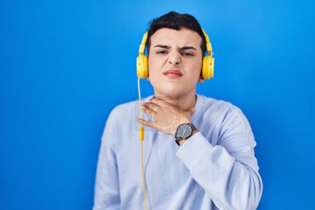 Foto de Persona no binaria escuchando música usando auriculares cortando la garganta con la mano como cuchillo, amenazan la agresión con violencia furiosa - Imagen libre de derechos
