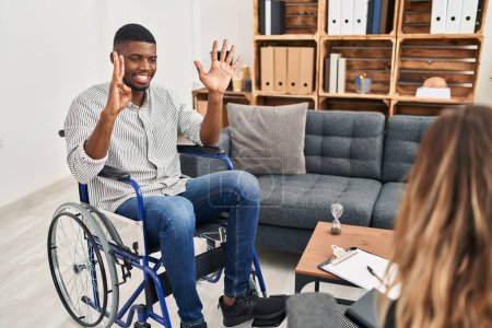 Photo for African american man doing therapy sitting on wheelchair showing and pointing up with fingers number eight while smiling confident and happy. - Royalty Free Image