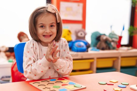 Foto de Adorable chica hispana jugando con matemáticas rompecabezas juego aplaudiendo manos en el jardín de infantes - Imagen libre de derechos