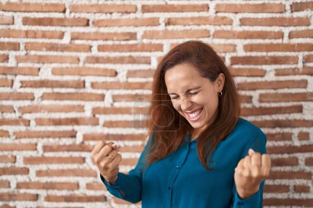 Téléchargez les photos : Femme brune debout sur le mur de briques très heureux et excité de faire geste gagnant avec les bras levés, souriant et criant pour le succès. concept de célébration. - en image libre de droit