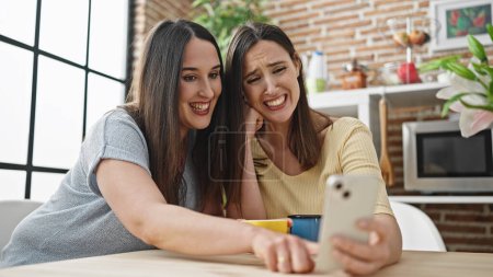 Photo for Two women drinking coffee watching video on smartphone at dinning room - Royalty Free Image