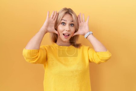 Téléchargez les photos : Jeune femme caucasienne portant un pull jaune souriant joyeux jeu jeter un coup d'oeil avec les mains montrant le visage. surpris et sortis - en image libre de droit