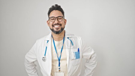 Téléchargez les photos : Jeune homme latin médecin souriant confiant debout sur fond blanc isolé - en image libre de droit