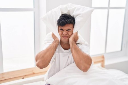 Photo for Young hispanic man covering ears for noise at bedroom - Royalty Free Image