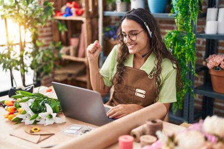 Photo for Young hispanic woman working at florist shop doing video call screaming proud, celebrating victory and success very excited with raised arm - Royalty Free Image
