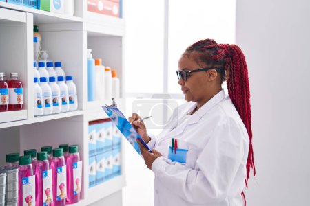 Foto de Farmacéutica afroamericana organiza estanterías en farmacia - Imagen libre de derechos