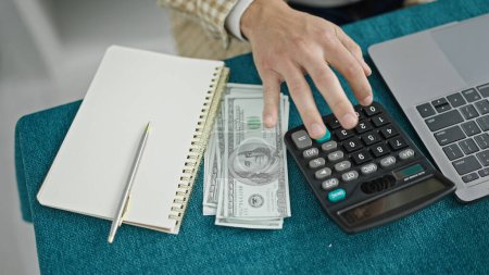 Photo for Young hispanic man counting dollars using calculator writing notes at dinning room - Royalty Free Image