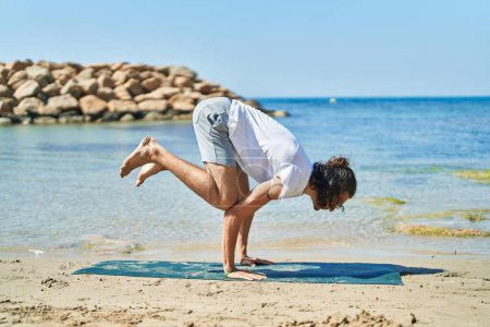 Photo for Young hispanic man doing yoga exercise at beach - Royalty Free Image