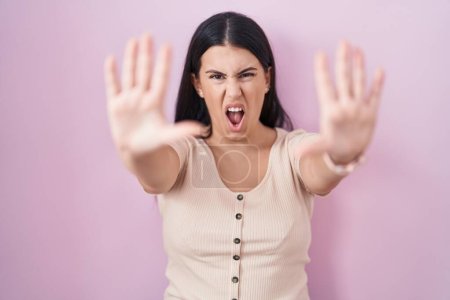 Téléchargez les photos : Jeune femme hispanique debout sur fond rose faisant geste d'arrêt avec les paumes des mains, expression de colère et de frustration - en image libre de droit