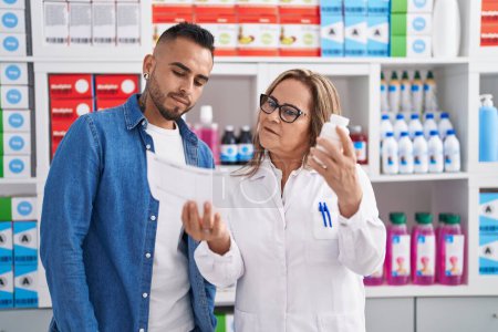 Téléchargez les photos : Man and woman pharmacist reading pills label bottle and prescription at pharmacy - en image libre de droit
