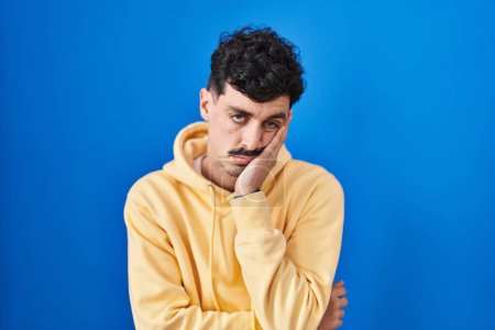 Foto de Hispanic man standing over blue background thinking looking tired and bored with depression problems with crossed arms. - Imagen libre de derechos