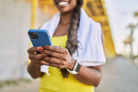 Téléchargez les photos : Femme afro-américaine portant des vêtements de sport à l'aide d'un smartphone dans la rue - en image libre de droit