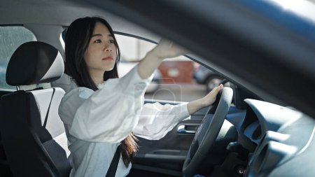 Foto de Young chinese woman touching rearview sitting on car at street - Imagen libre de derechos
