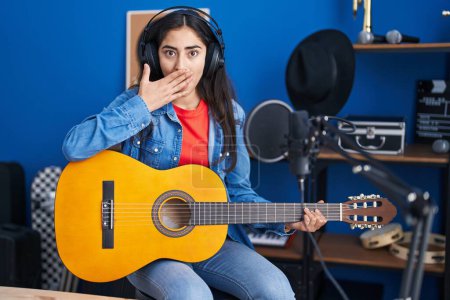 Photo for Young teenager girl playing classic guitar at music studio covering mouth with hand, shocked and afraid for mistake. surprised expression - Royalty Free Image