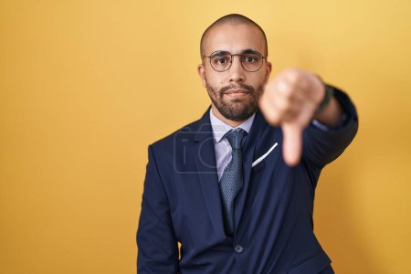 Photo for Hispanic man with beard wearing suit and tie looking unhappy and angry showing rejection and negative with thumbs down gesture. bad expression. - Royalty Free Image